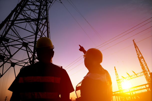 zwei Arbeiter beobachten den Strommast und das Umspannwerk bei Sonnenuntergang - Foto, Bild