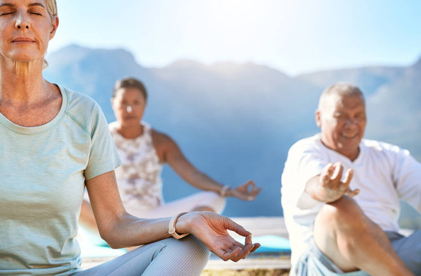 Oudere mannen en vrouwen die in lotuspositie zitten en meditatie beoefenen tijdens yoga-oefening in de natuur en zich kalm voelen. Gepensioneerden met een gezonde actieve levensstijl. - Foto, afbeelding