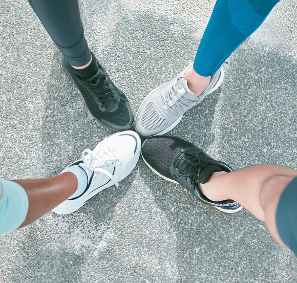Gros plan d'un groupe diversifié d'athlètes d'en haut portant des chaussures de sport et debout avec les pieds en cercle pour l'unité, le soutien et la solidarité. Chaussures de coureurs dédiés se réunissant dans hudd. - Photo, image