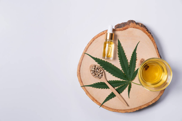 Zestaw zalegalizowanej marihuany zawiera zielony liść konopi, olej CBD w butelce z pokrywą kroplomierza i szklaną miską oraz nasiona konopi wyświetlane na drewnianej płycie. - Zdjęcie, obraz