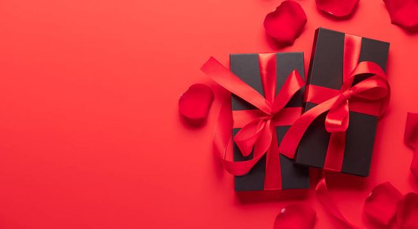 Tarjeta de San Valentín con cajas de regalo y pétalos de flor de rosa. Sobre fondo rojo con espacio para tus saludos - Foto, imagen