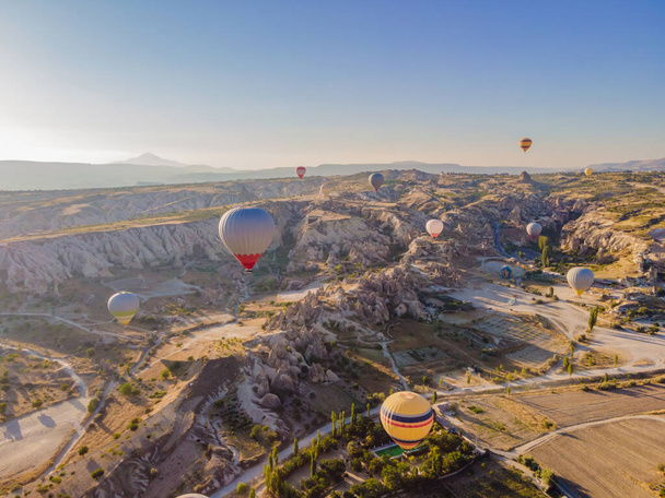 Colorful hot air balloons flying over at fairy chimneys valley in Nevsehir, Goreme, Cappadocia Turkey. Spectacular panoramic drone view of the underground city and ballooning tourism. High quality. - Foto, Imagen