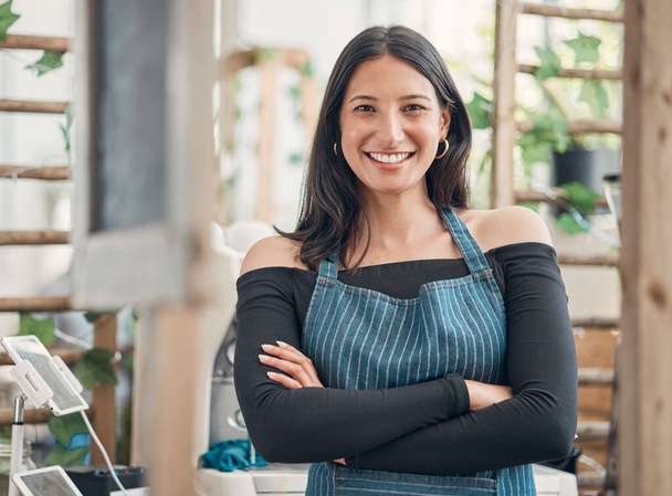 Portrait of one happy young hispanic waitress standing with her arms crossed in a store or cafe. Friendly woman and coffeeshop owner managing a successful restaurant startup. - Photo, Image