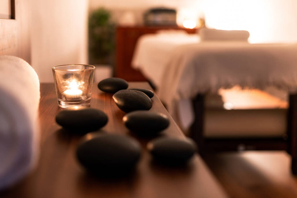 Towel, candle and lava rocks in spa salon. Bluerred. massage table in the background - Fotoğraf, Görsel