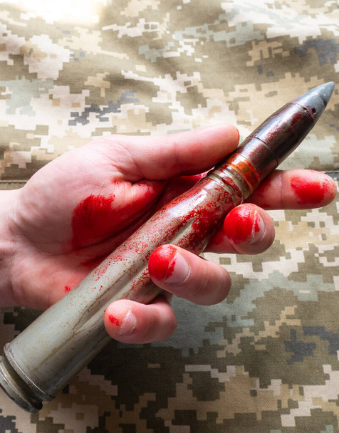Shell missiles with blood in mans hand on khaki jacket background. No war, army concept. - Zdjęcie, obraz