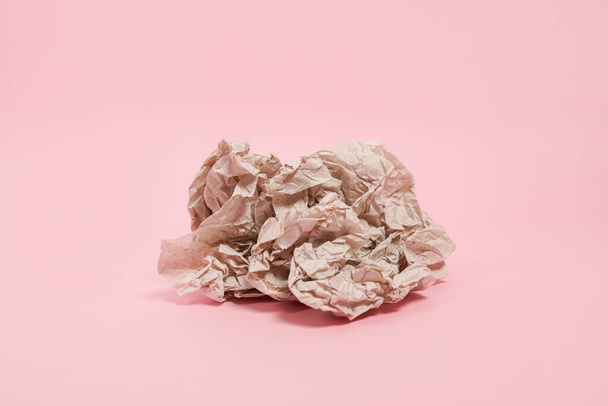 Смятый бумажный шар, лежащий на розовом фоне - Фото, изображение