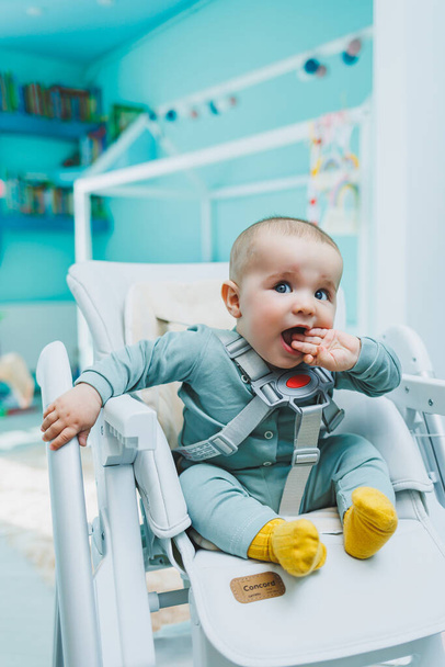 Ein kleiner gutaussehender Junge sitzt zum Füttern in einem Hochstuhl. Kinderküchenstuhl zum Essen. Kindermöbel - Foto, Bild