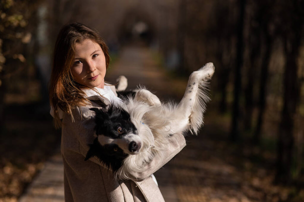 Caucasian woman holding a border collie in her arms while walking in the autumn park. Portrait of a girl with a dog - Photo, Image