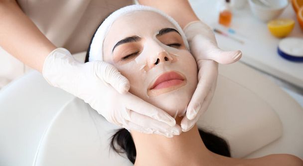 Косметолог надевает маску на лицо женщины в салоне красоты - Фото, изображение