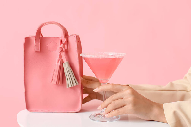 ピンクの女性のカクテルとスタイリッシュなハンドバッグを持っている女性に白いテーブルの上に背景色、クローズアップ - 写真・画像