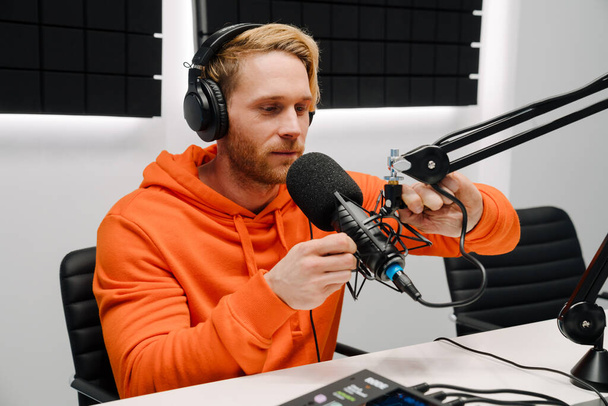 Happy young male radio host using microphone and headphones while broadcasting in studio - Fotografie, Obrázek