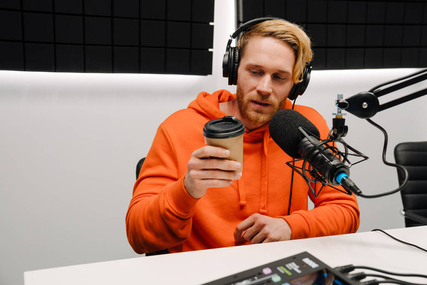Happy young male radio host using microphone and headphones while broadcasting in studio - Фото, зображення