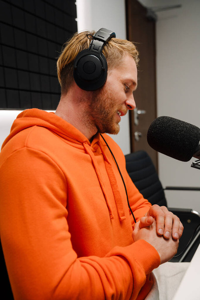 Happy young male radio host using microphone and headphones while broadcasting in studio - Valokuva, kuva