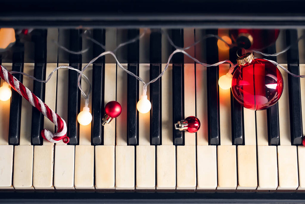 Red Christmas balls with glowing lights on piano keys, closeup - Photo, Image