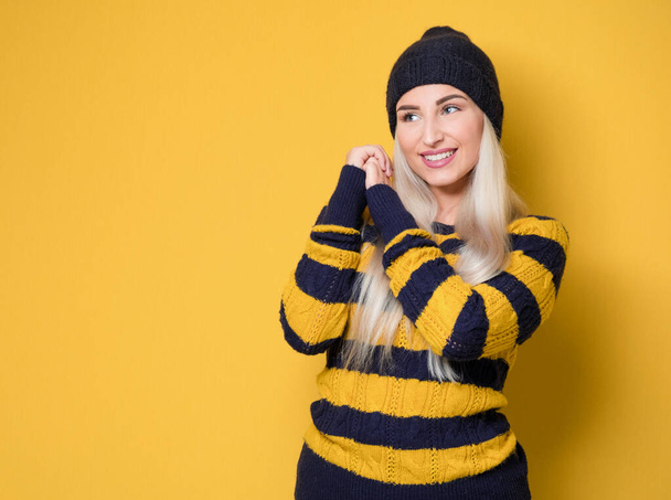 Portrait of joyful girl. Happy young woman with smile face expression, model wearing woolen cap and sweater, isolated on yellow background. Studio shot - Photo, Image