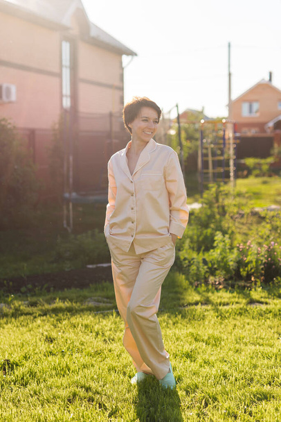 Vrolijke vrouw in huis te dragen pyjama zomer buiten achtertuin in huis - slaap- en huishoudkleding - Foto, afbeelding