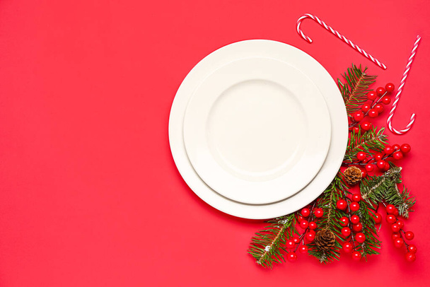 Białe talerze z gałęziami bożonarodzeniowymi, żurawiną i cukierkami na czerwonym tle - Zdjęcie, obraz