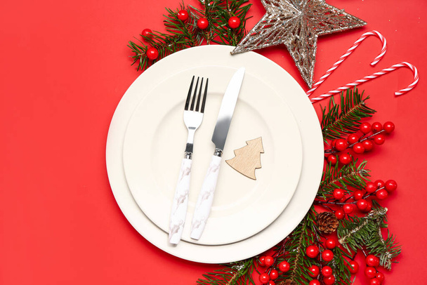 Apparecchiatura della tavola con rami di Natale, bastoncini di mirtillo e caramelle su sfondo rosso - Foto, immagini
