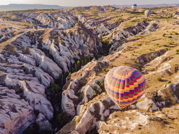 Colorful hot air balloons flying over at fairy chimneys valley in Nevsehir, Goreme, Cappadocia Turkey. Spectacular panoramic drone view of the underground city and ballooning tourism. High quality. - Фото, изображение