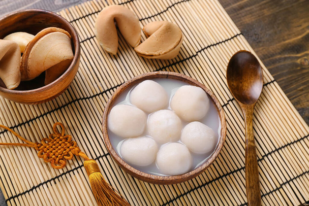 Bamboo mat with bowl of tangyuan and fortune cookies on wooden background. Dongzhi Festival - Photo, Image