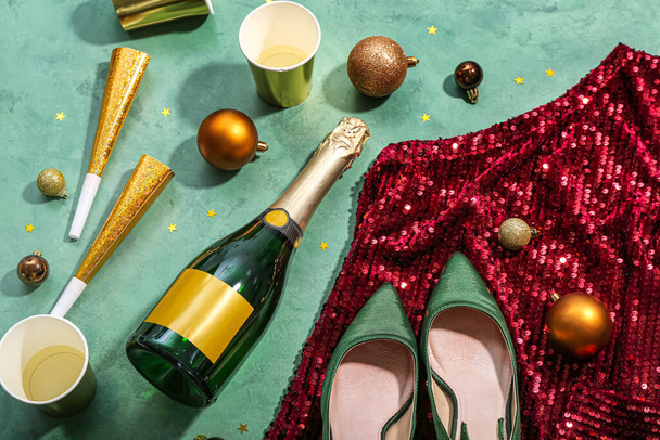Bottle of champagne, cups, Christmas balls, party horns and dress on green background - Photo, Image