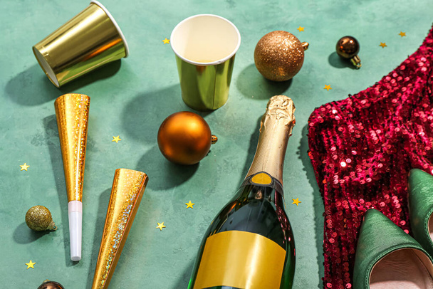 Flasche Champagner, Tassen, Weihnachtskugeln, Partyhörner und Kleid auf grünem Hintergrund - Foto, Bild