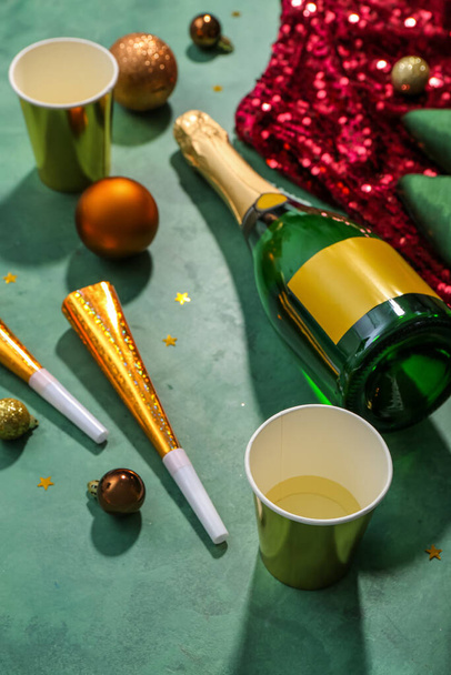 Fles champagne, bekers, kerstballen, feesthoorns en jurk op groene achtergrond - Foto, afbeelding