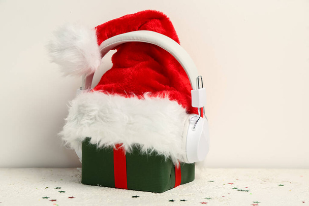 Headphones with Christmas gift and Santa hat on light background - Fotoğraf, Görsel