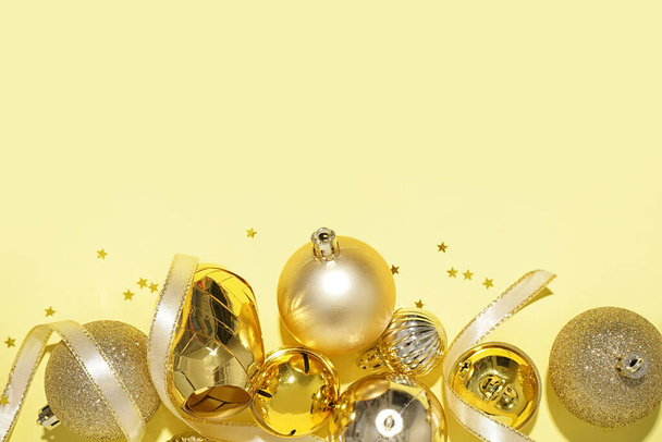 Χρυσές Χριστουγεννιάτικες μπάλες με καμπάνες και κορδέλα σε κίτρινο φόντο - Φωτογραφία, εικόνα