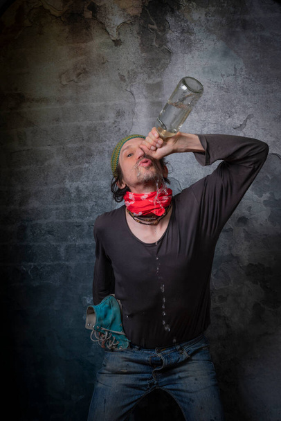 Sale homme alcoolique avec bouteille de vodka près de vieux mur de couleur de pierre - Photo, image