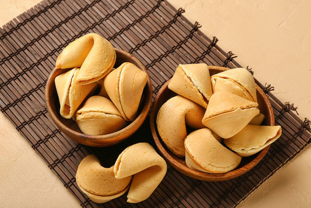 Bamboo mat with bowls of fortune cookies on beige background, closeup - Photo, Image