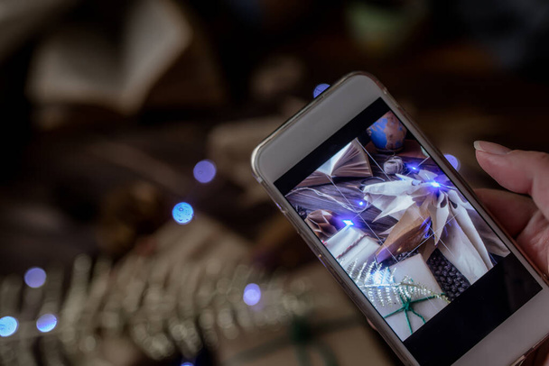 Телефон находится в руках блогера. Фотография для блога о процессе упаковки ремесленных подарков на Рождество и изготовления бумажной звезды из мешков. - Фото, изображение