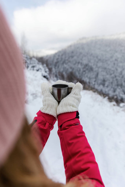 Traveler woman holding cup of coffee on the background of the mountains. Adventure, travel, winter concept. - Photo, Image