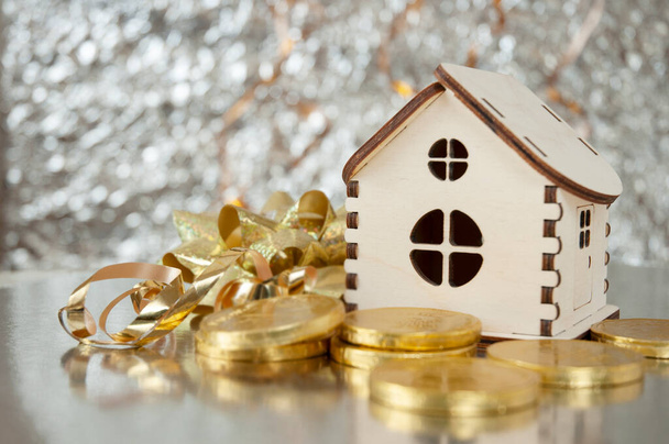 dřevěný dům model, zlaté čokoládové mince a novoroční dekorace na zářícím pozadí s kopírovacím prostorem, vánočním pozadím, Bohatství koncept. Nový rok prodej pro nové domy koncept - Fotografie, Obrázek
