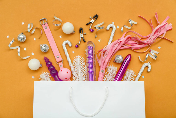 Bolsa de compras con juguetes sexuales y decoración de Navidad sobre fondo naranja - Foto, Imagen