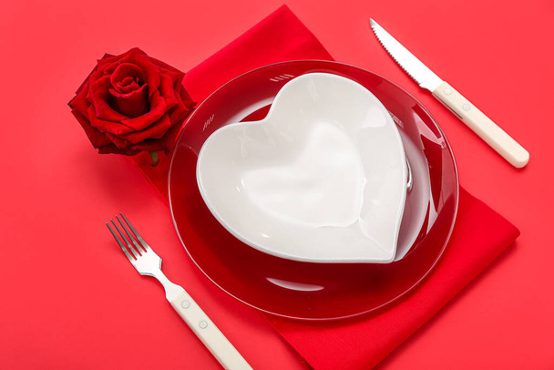 Table setting for Valentine's Day with heart shaped plate and rose on red background - Zdjęcie, obraz