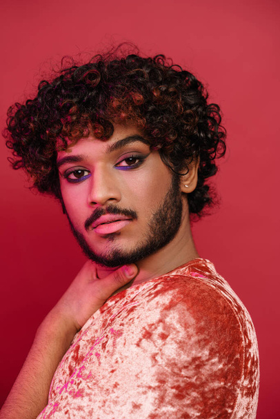 Young curly man with makeup posing and looking at camera isolated over pink background - Foto, Bild