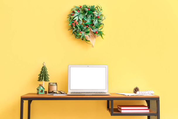Laptop met kerstspeelgoed en kaars op tafel bij gele muur - Foto, afbeelding