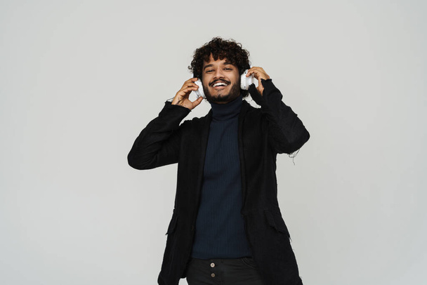 Young adult indian smiling curly man in headphones over isolated grey background - Valokuva, kuva