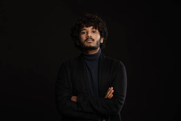 Young handsome indian curly serious man standing arms folded looking at camera over isolated dark background - Φωτογραφία, εικόνα