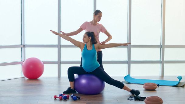 Terhes nő megy a sport a tornateremben. Személyi Fitness edző segít gyakorolni a terhes nők számára. Felkészítem a testet a szülésre. Terhesség, Sport és egészség koncepció. - Fotó, kép