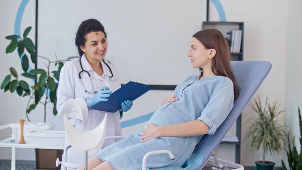 Ευτυχισμένη Έγκυος Γυναίκα Επισκεφθείτε Γυναικολόγος Γιατρός στην Ιατρική Κλινική για Σύμβουλο Εγκυμοσύνης. Γυναίκα γιατρός Εξετάστε έγκυος νεαρή μητέρα για να ελέγξετε μέχρι την υγεία της. Συμβουλευτική των εγκύων στην Κλινική. - Φωτογραφία, εικόνα