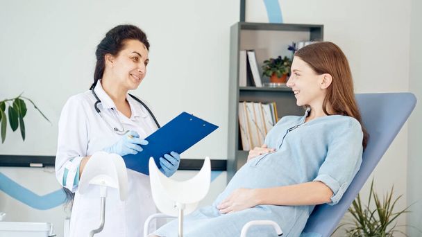 Happy Pregnant Woman Visit Gynecologist Doctor at the Medical Clinic for Pregnancy Consultant. Female Doctor Examine Pregnant Young Mother to Check Up Her Healthcare. Consulting of Pregnant at Clinic. - Φωτογραφία, εικόνα