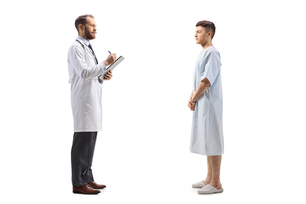 Full length profile shot of a male doctor and a young patient standing and talking isolated on white background - 写真・画像