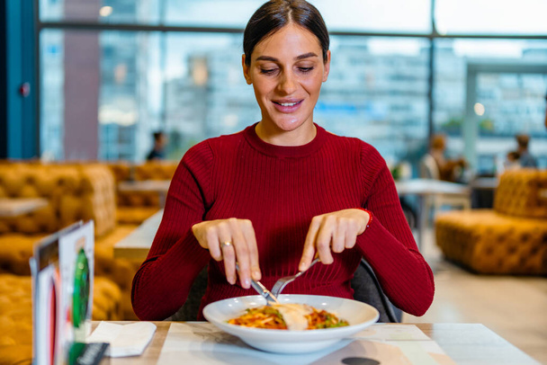 Fiatal nő mosolyog és ebédel, a hajával a zsemlében. Fiatal nő eszik tészta az étteremben a városi háttér - Fotó, kép