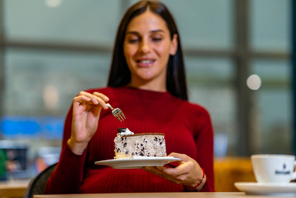 Closeup of a pregnant woman smiling and having desert. Smiling young woman is enjoying a piece of chocolate cake. Woman in coffee shop sitting at table eating slice ff cake - Foto, afbeelding