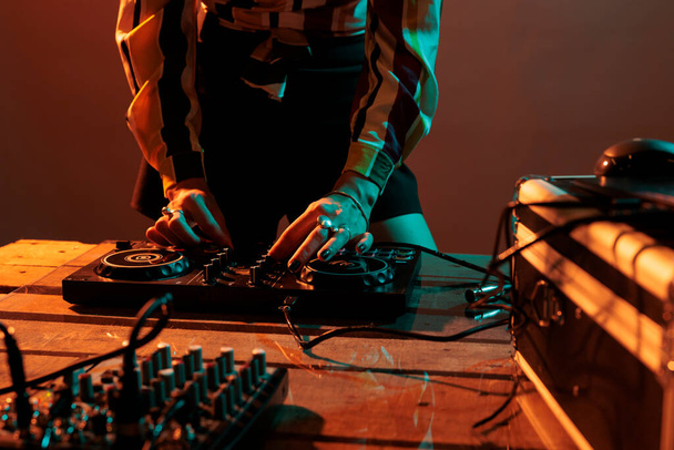 Woman performer mixing techno music on turntables, playing record mix sounds on audio dj instrument and stereo equipment. Enjoying nightclub party with stage production in studio. - Foto, imagen