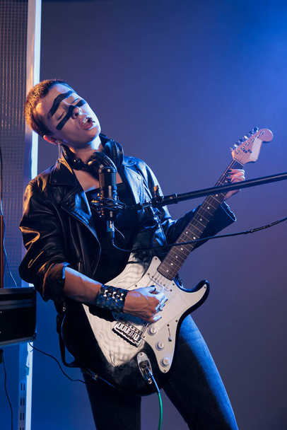 Рок-звезда, играющая на гитаре, чувствующая хэви-метал и наслаждающаяся альтернативным панк-роком. Крутой артист с инструментом и пением, в кожаной куртке. - Фото, изображение