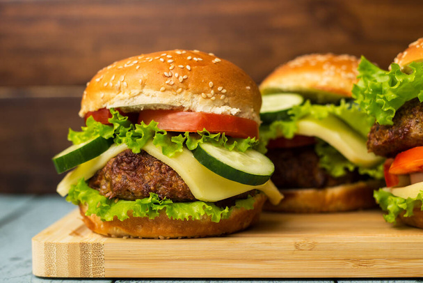 Burgers with beef meat, cheese and lettuce, served on cutting board - Foto, Imagen