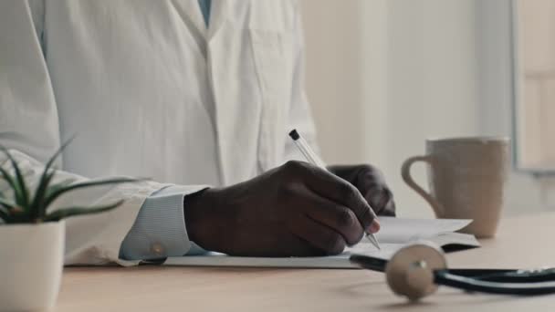 Felismerhetetlen férfi orvos terapeuta kardiológus visel orvosi kabát ül az íróasztalnál írni diagnosztizálni notebook tervezés munkanap írja fel a gyógyszer eredmények írása szakmai ajánlás - Felvétel, videó